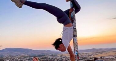 Woman performing a handstand on a flagpole in Cappadocia, Turkey.