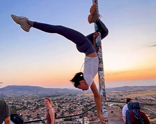 Woman performing a handstand on a flagpole in Cappadocia, Turkey.