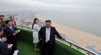 Kim Jong Un and his daughter overlooking a beach from a balcony.