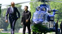 Volodymyr Zelensky and Friedrich Merz walking in a garden, with a helicopter in the background.