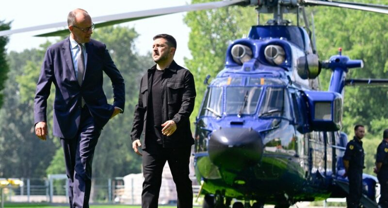 Volodymyr Zelensky and Friedrich Merz walking in a garden, with a helicopter in the background.