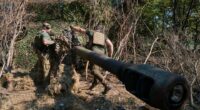 Ukrainian soldiers camouflage a howitzer.