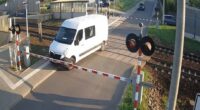A white van narrowly avoids being hit by a train at a railway crossing.