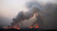Wildfire smoke billows over a landscape.