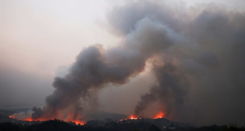 Wildfire smoke billows over a landscape.