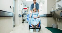 Pregnant woman in a wheelchair being pushed by a man down a hospital corridor.