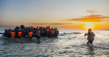 Migrants board a small inflatable boat in the English Channel at sunrise.