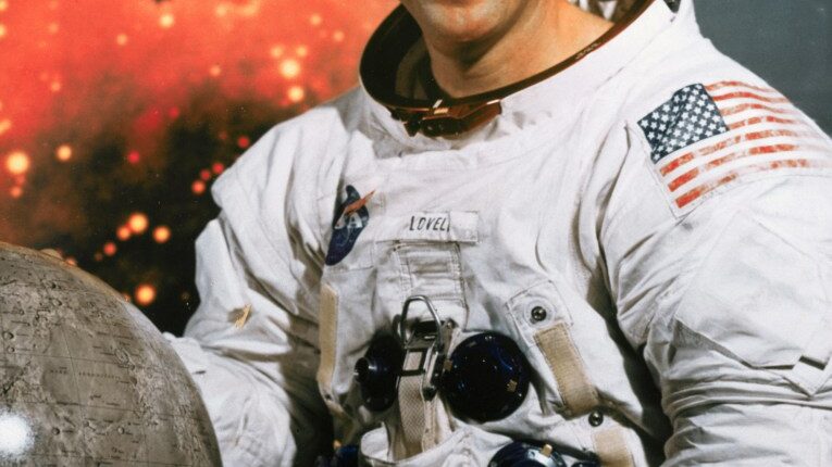 Portrait of Jim Lovell, Apollo 13 commander, in a spacesuit holding a moon globe.
