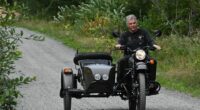 Man riding a Ural motorcycle with a sidecar on a gravel road.