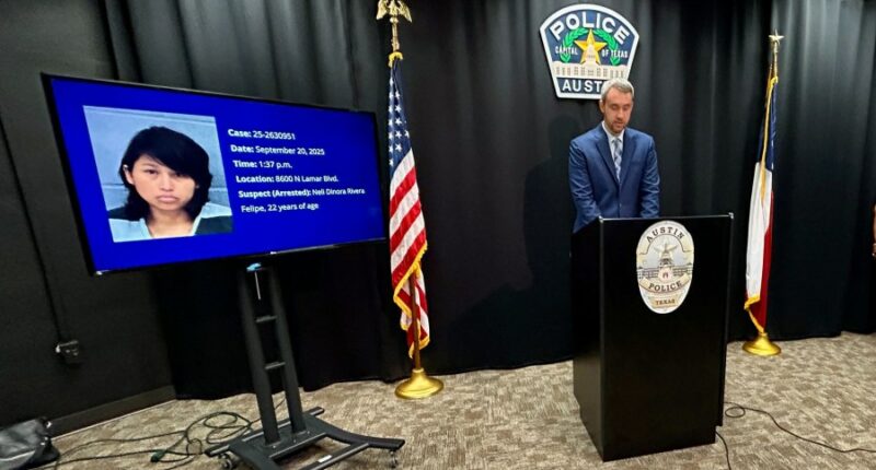 Austin police official stands at podium next to TV screen showing arrested suspect's mugshot