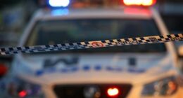 Police Tape in the foreground with a police car with it's lights on in the background