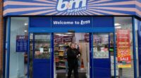 Shoppers exit the B&M store in London, with sale and opening hours signs visible on the entrance doors