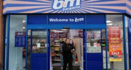 Shoppers exit the B&M store in London, with sale and opening hours signs visible on the entrance doors