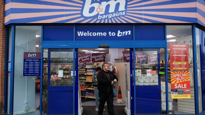 Shoppers exit the B&M store in London, with sale and opening hours signs visible on the entrance doors