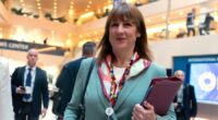 Rachel Reeves walks inside the IMF headquarters holding a folder, wearing a teal suit and colourful scarf, during the G20 meeting.