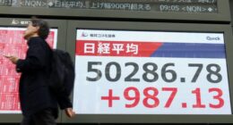 A person walks past a large electronic display in Tokyo showing the Nikkei Stock Average surpassing 50,000 points.