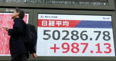 A person walks past a large electronic display in Tokyo showing the Nikkei Stock Average surpassing 50,000 points.