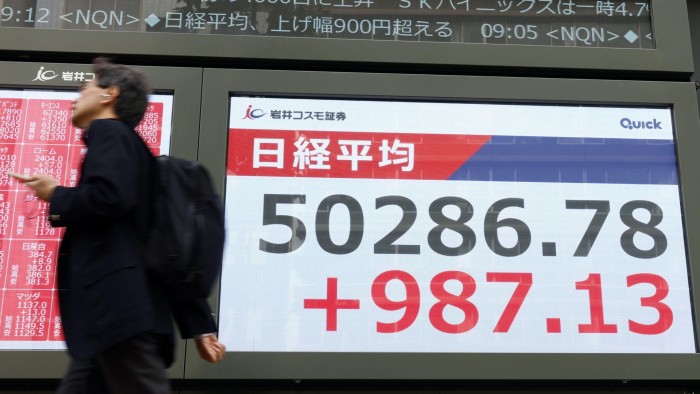 A person walks past a large electronic display in Tokyo showing the Nikkei Stock Average surpassing 50,000 points.
