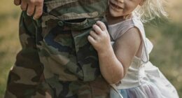 A heartwarming moment between a soldier parent and their young daughter during a reunion outdoors. The child, dressed in a fairy princess dress, clings affectionately to the parent in military camouflage uniform. The scene is filled with emotion, bonding, and love, captured in warm natural sunlight.