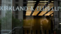 Signage for Kirkland & Ellis LLP is displayed on the glass entrance of a building, with people visible in silhouette inside.