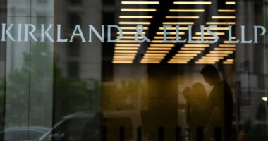 Signage for Kirkland & Ellis LLP is displayed on the glass entrance of a building, with people visible in silhouette inside.