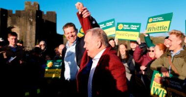 Rhun ap Iorwerth lifts Lindsay Whittle’s arm in celebration, surrounded by supporters holding Plaid Cymru signs.