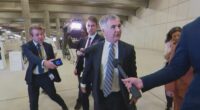 Optus CEO Stephen Rue, surrounded cameras and journalists ahead of his meeting with Anika Wells in Parliament House.