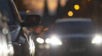 Cars in traffic during dusk, showcasing headlights and city lights, with a blurred background reflecting urban life
