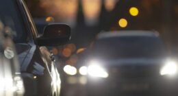 Cars in traffic during dusk, showcasing headlights and city lights, with a blurred background reflecting urban life