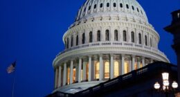 The dome of the US Capitol is illuminated at dusk with an American flag and street lamps visible in the foreground.