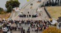 EDS NOTE: OBSCENITY - Protesters block the entrance to Coast Guard Base Alameda shortly after a caravan of U.S. Customs and Border Protection personnel arrived on Thursday, Oct. 23, 2025, in Oakland, Calif. (AP Photo/Noah Berger)