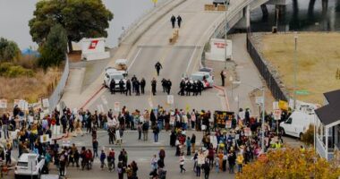 EDS NOTE: OBSCENITY - Protesters block the entrance to Coast Guard Base Alameda shortly after a caravan of U.S. Customs and Border Protection personnel arrived on Thursday, Oct. 23, 2025, in Oakland, Calif. (AP Photo/Noah Berger)