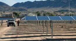 John Gatlin of Greenbotics walks between rows of solar panels at a solar generating station, with a truck nearby.