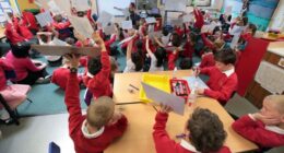 Children in red uniforms hold up whiteboards with answers during a primary school mathematics lesson.