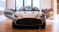 The 2025 Aston Martin Vanquish displayed indoors with both doors open, viewed from the front.