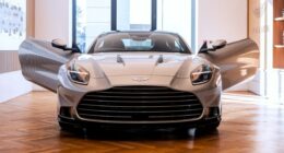 The 2025 Aston Martin Vanquish displayed indoors with both doors open, viewed from the front.