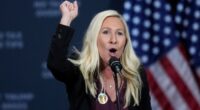 Rep. Marjorie Taylor Greene speaks at a podium with her fist raised, with American flags in the background.