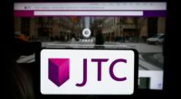 JTC plc logo displayed on a smartphone screen held in front of a blurred JTC website.