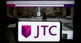 JTC plc logo displayed on a smartphone screen held in front of a blurred JTC website.