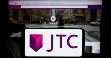 JTC plc logo displayed on a smartphone screen held in front of a blurred JTC website.