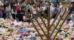 A Hanukkah menorah stands by a floral tribute as people gather to pay their respects near the Bondi Pavilion at Bondi Beach today.