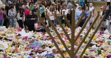 A Hanukkah menorah stands by a floral tribute as people gather to pay their respects near the Bondi Pavilion at Bondi Beach today.