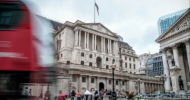 The Bank of England building with a blurred red double-decker bus passing in front and people gathered outside.