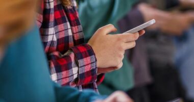 Close-up group of teenagers using mobile phones in school corridor