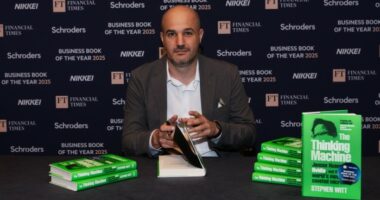 Stephen Witt sits at a table with stacks of his book, ‘The Thinking Machine’, preparing to sign a copy.
