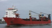 The Russian cargo ship Adler sails on the water, showing a red hull, white superstructure, and onboard cranes.