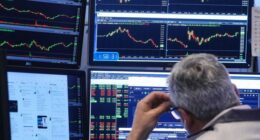 A trader looks at multiple computer monitors displaying stock charts and market data on the floor of the New York Stock Exchange.