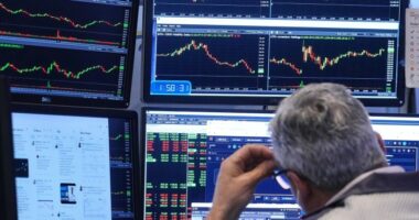 A trader looks at multiple computer monitors displaying stock charts and market data on the floor of the New York Stock Exchange.