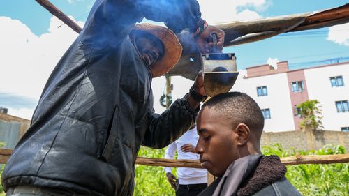 Barber and viral content creator Safari Martins, demonstrates one of his inventive shaving methods using an iron box while grooming Ian Njenga in Kiambu, Kenya, Wednesday, Nov. 26, 2025. (AP Photo/Andrew Kasuku)