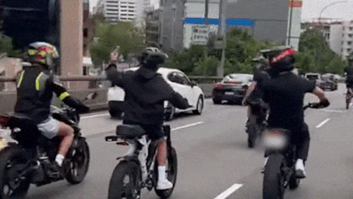 Group of young people riding e-bikes in Sydney peak hour traffic.